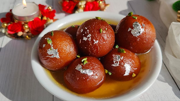 Gulab Jamun (Hindistan)

Hindistan’ın sevilen tatlısı gulab jamun, gül suyu şerbetiyle ıslatılmış yuvarlak hamur toplarıdır. Khoa (kurutulmuş süt), un ve kabartma tozuyla hazırlanan hamur, kızartılıp şeker, kakule ve gül suyu şerbetine batırılır. Pers işgalcilerinin yanında buna çok benzer bir tatlı getirdiği bilinir. Bu yüzden Pers mutfağından geldiği kabul görür. “Gulab” Farsçada gül, “jamun” ise yerel bir meyveyi ifade eder. Moğol döneminde Hindistan’a ulaştığına inanılır ve bugün festivallerde sıkça tüketilir.